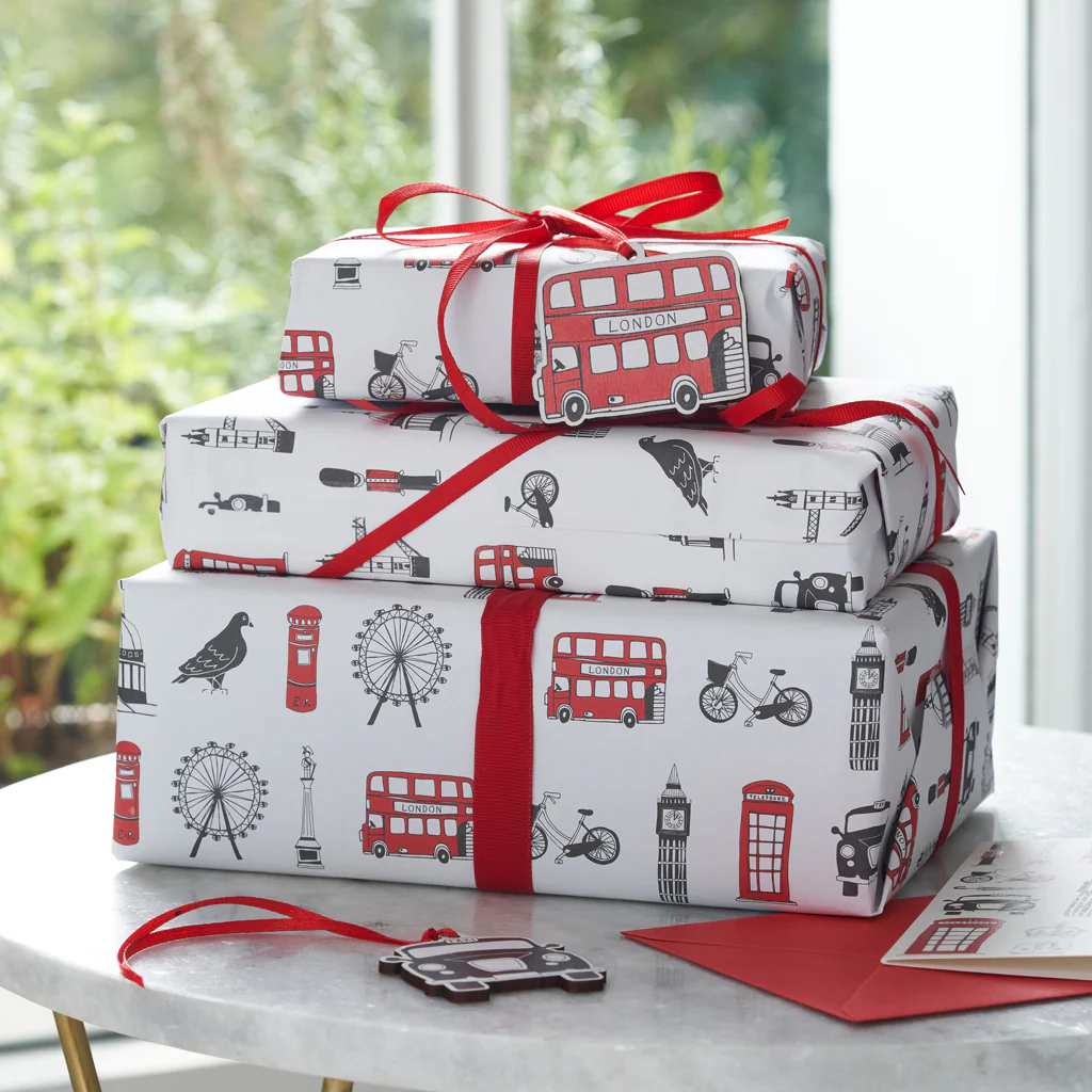 Gift boxes wrapped in London-themed paper with red ribbons and city icons like buses and Big Ben